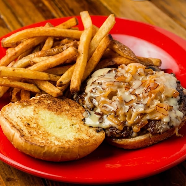 Open-faced burger with melted cheese and caramelized onions, served with fries on a red plate.