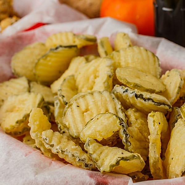 A red basket filled with crispy fried pickle chips, lined with white paper.