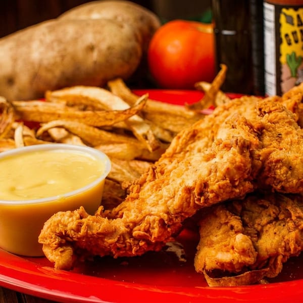 Crispy fried chicken tenders, golden french fries, and a side of dipping sauce on a red plate.