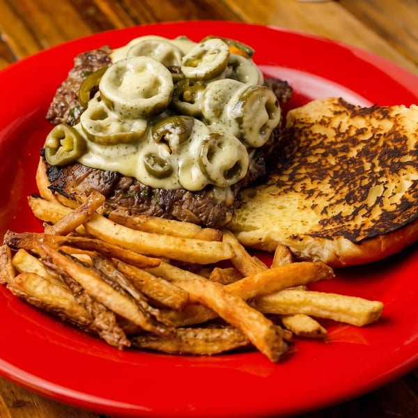 Open-faced burger with melted cheese and jalapeños, served with fries on a red plate.