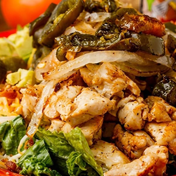 Grilled chicken, sautéed onions, and peppers on a bed of lettuce with cheese and avocado.
