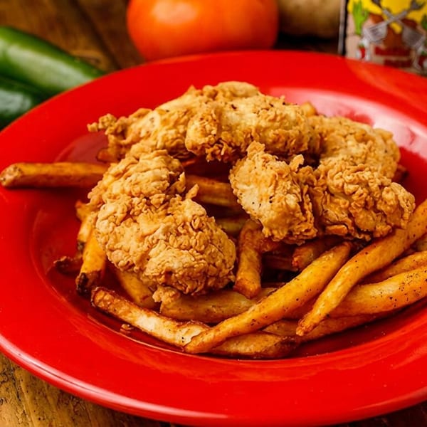 Crispy fried chicken tenders and seasoned french fries on a vibrant red plate, with jalapeños and tomato.
